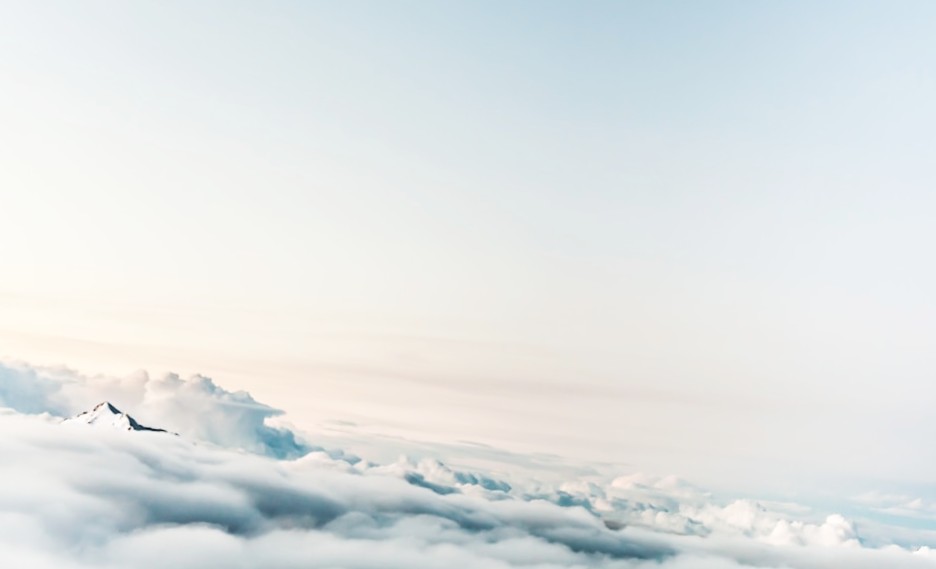 Mountain peak rising above a thick blanket of white clouds under a pale dawn sky
